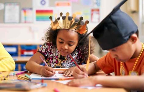 Two young children wearing costumes and engaged in a creative art activity in a classroom.