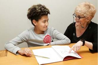 a young boy, and a lady sat at a table smiling doing school work