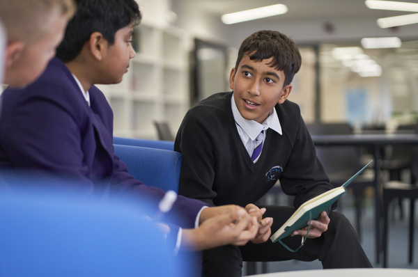 Three students sitting in a classroom, talking in a group about a piece of work