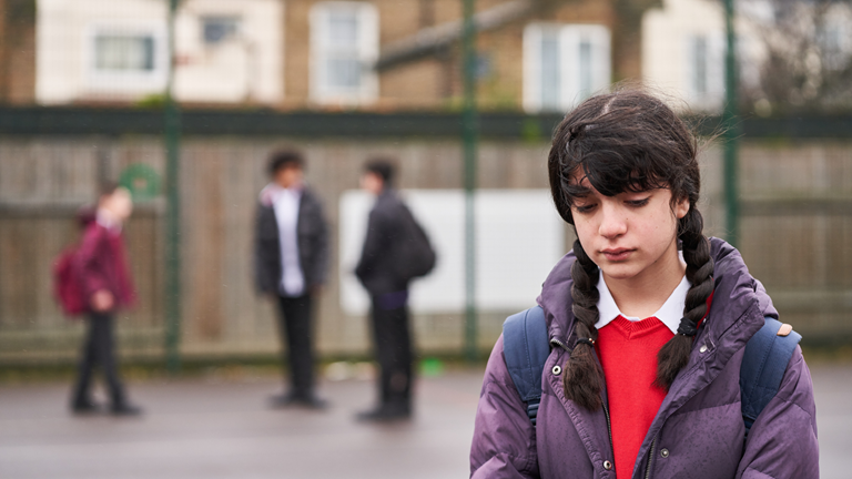 Young teenage girl stood alone in playground, looking sad