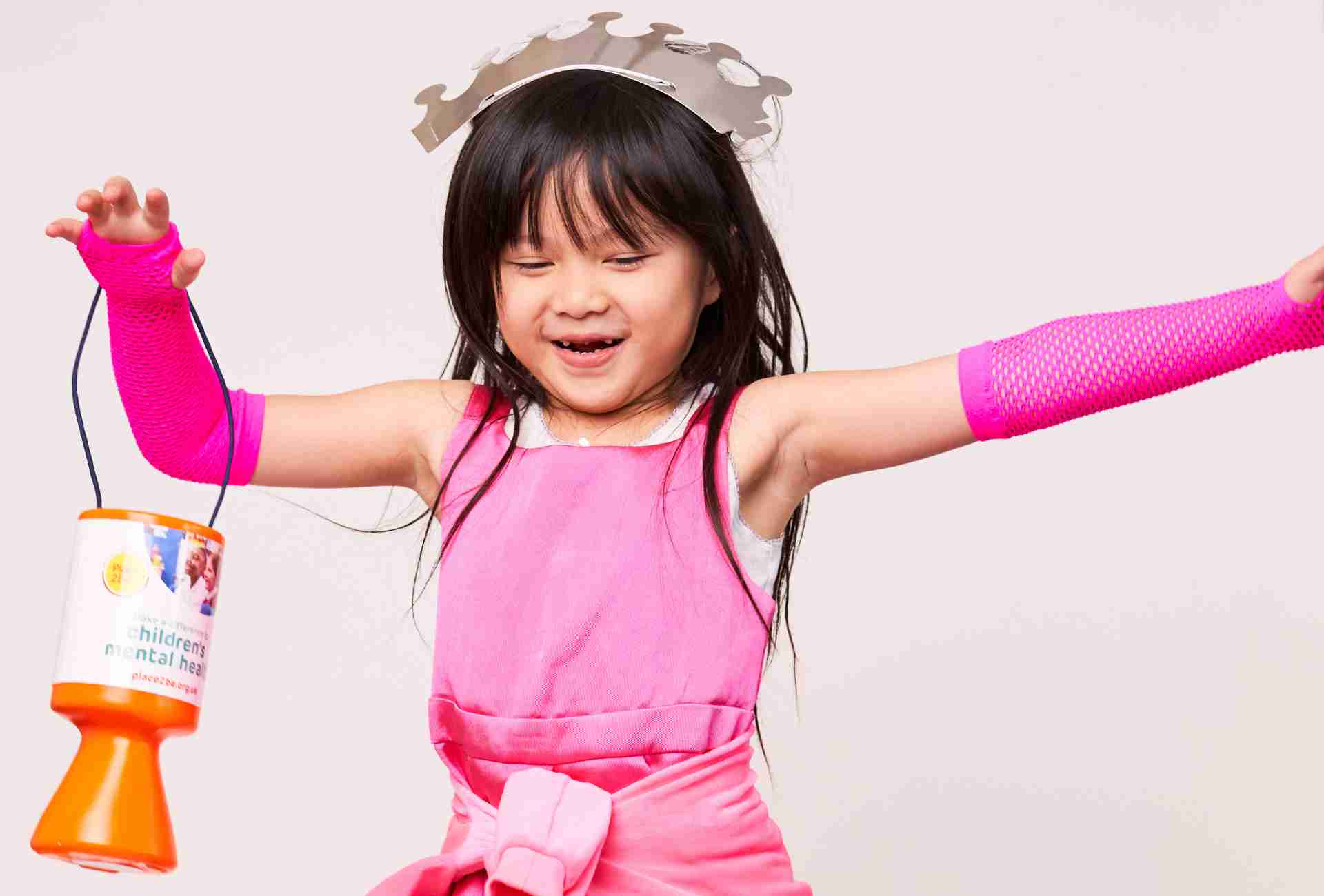 young girl in pink dress with a crown twirling holding a Place2Be donation tin