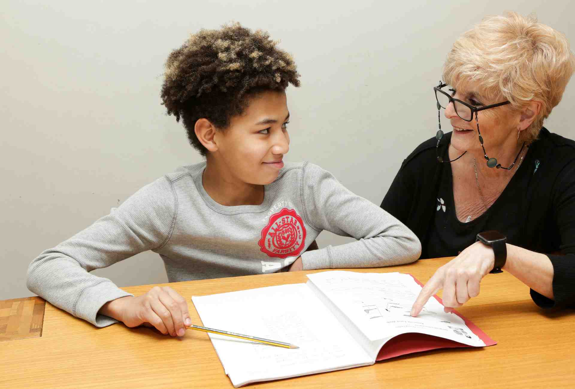 a young boy and a lady sitting at a table, smiling and doing work