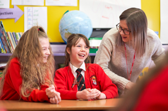 Teacher with two primary age female students, laughing at desk