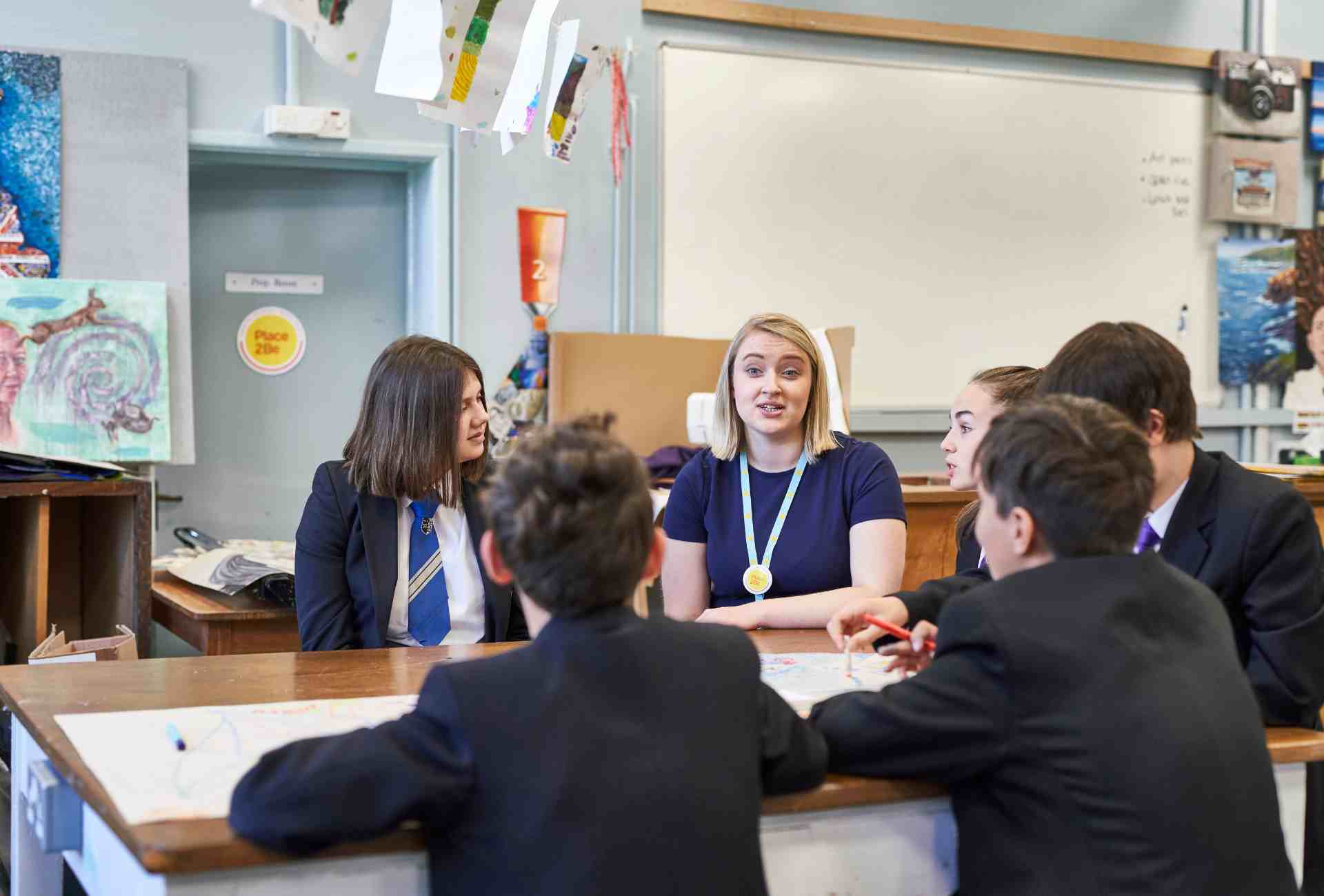 Group of secondary school students talking round a table with a member of staff